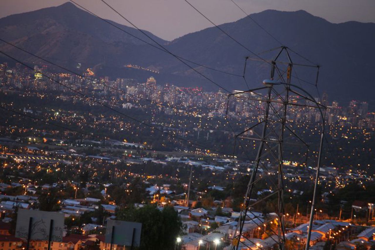 Imagen nocturna de ciudad con torre de alta tension